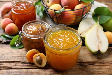 Photo of Jars with different jams and fresh fruits on wooden table