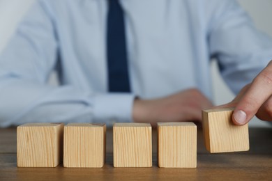Photo of Businessman arranging blank cubes on wooden table, closeup. Space for text