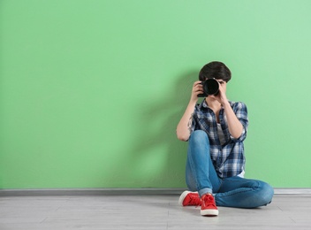 Photo of Young female photographer with camera near color wall
