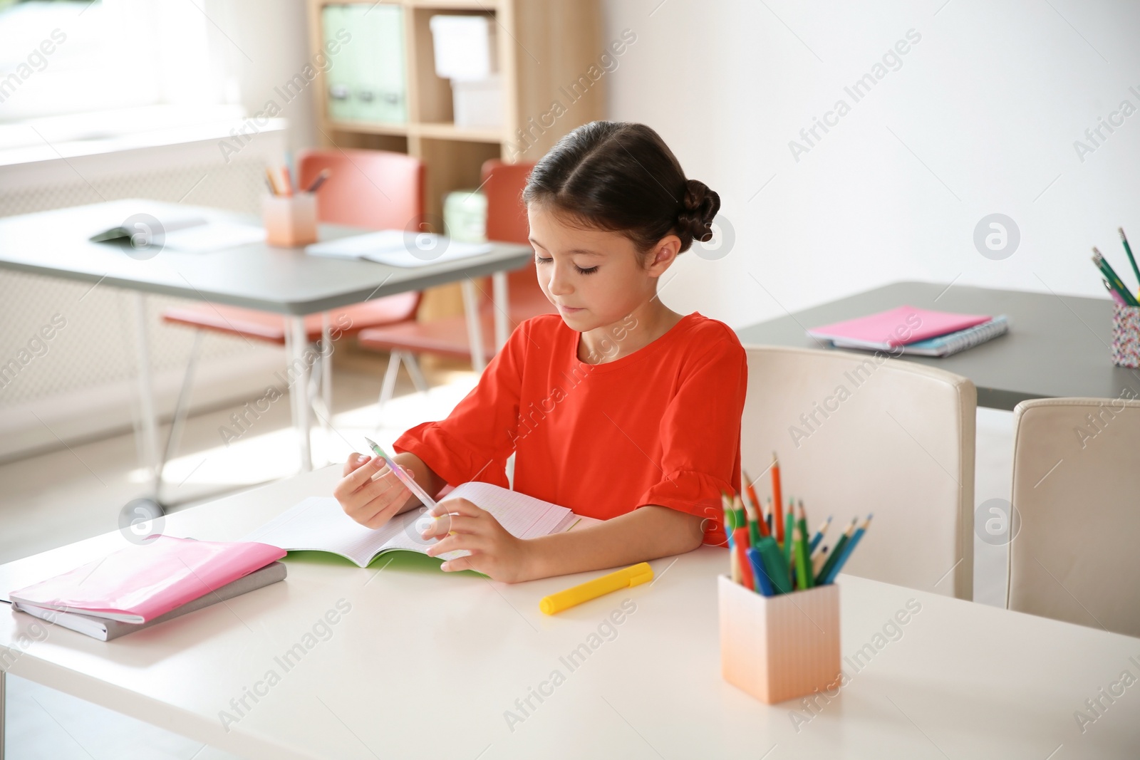 Photo of Cute little child doing assignment at desk in classroom. Elementary school