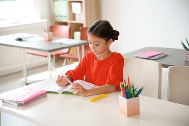 Photo of Cute little child doing assignment at desk in classroom. Elementary school