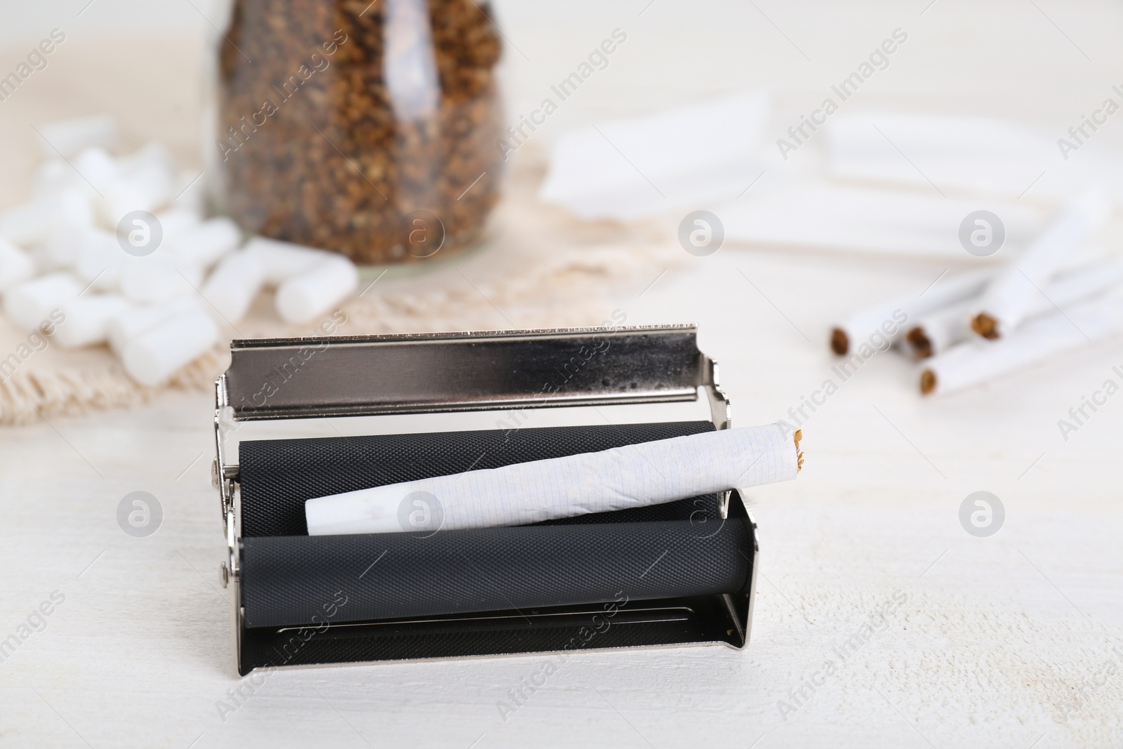 Photo of Manual roller with hand rolled tobacco cigarette on white wooden table, closeup