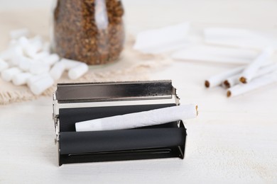 Photo of Manual roller with hand rolled tobacco cigarette on white wooden table, closeup