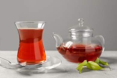Photo of Glass of traditional Turkish tea and pot on light grey table, closeup