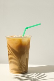 Photo of Plastic takeaway cupdelicious iced coffee on white table under sunlight