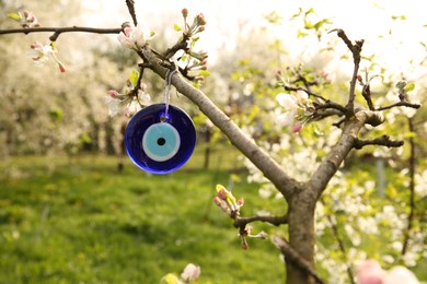 Photo of Evil eye amulet hanging on blossoming spring tree outdoors, closeup