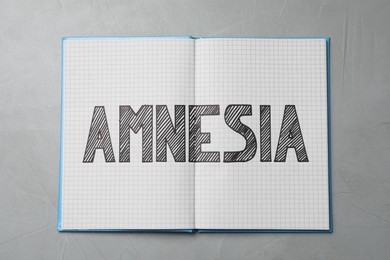 Notebook with word Amnesia on light grey table, top view