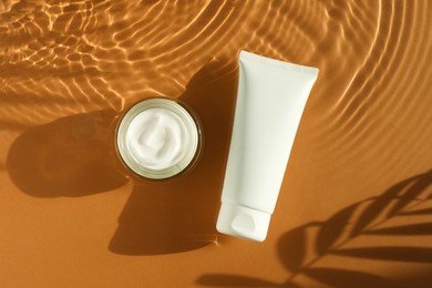 Photo of Tube and jar with moisturizing cream in water on orange background, top view