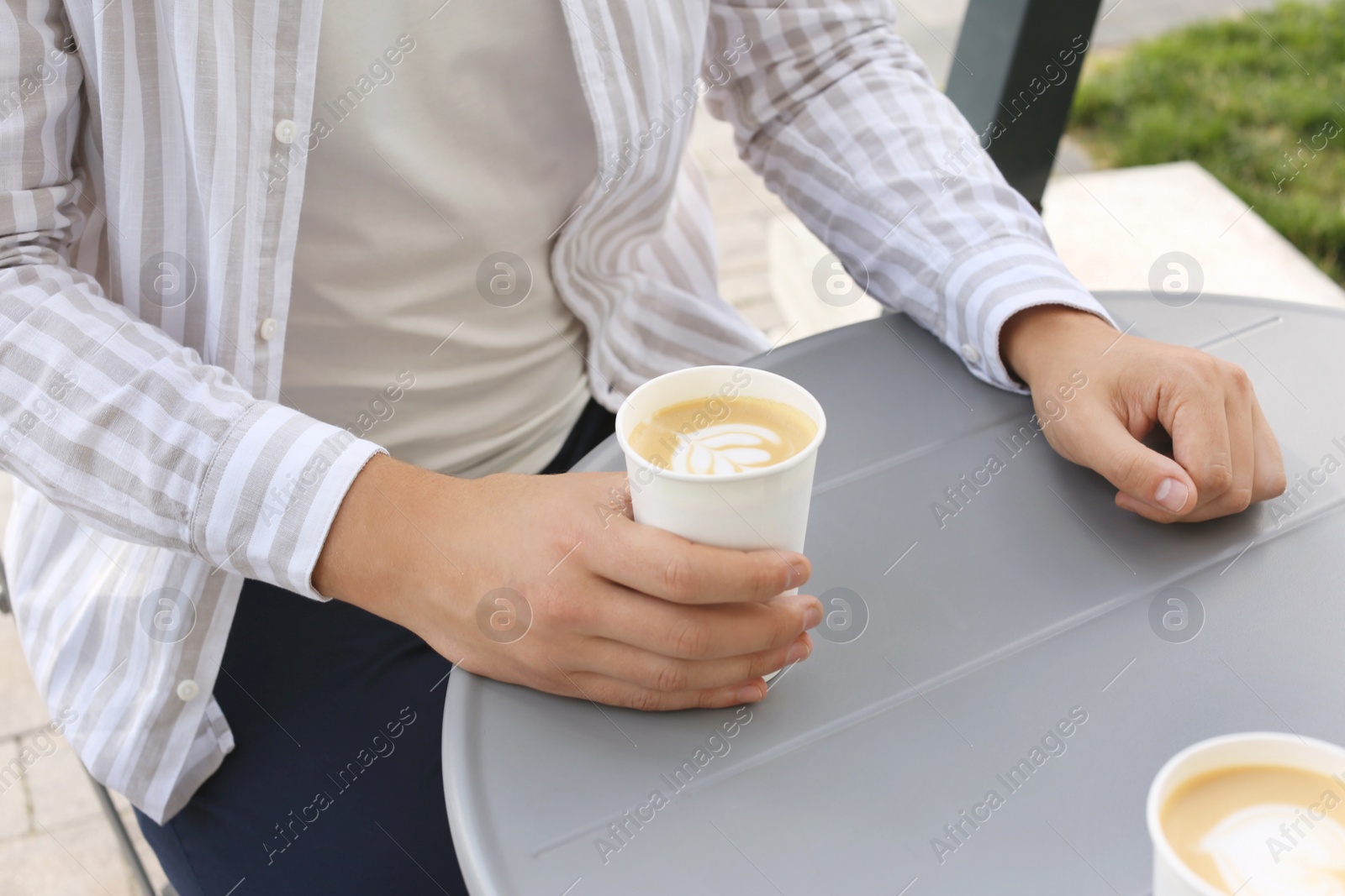 Photo of Coffee to go. Man with paper cup of drink at grey table outdoors, closeup