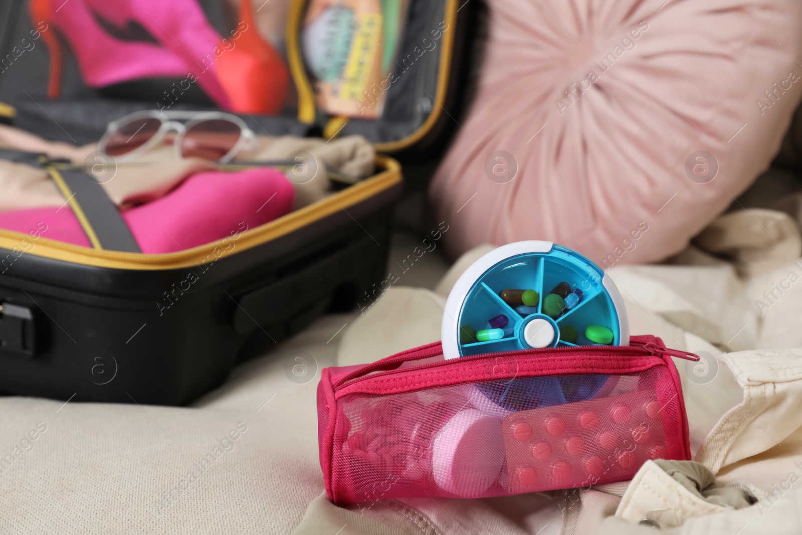 Photo of Pouch with different medicaments and pill box near packed suitcase on sofa