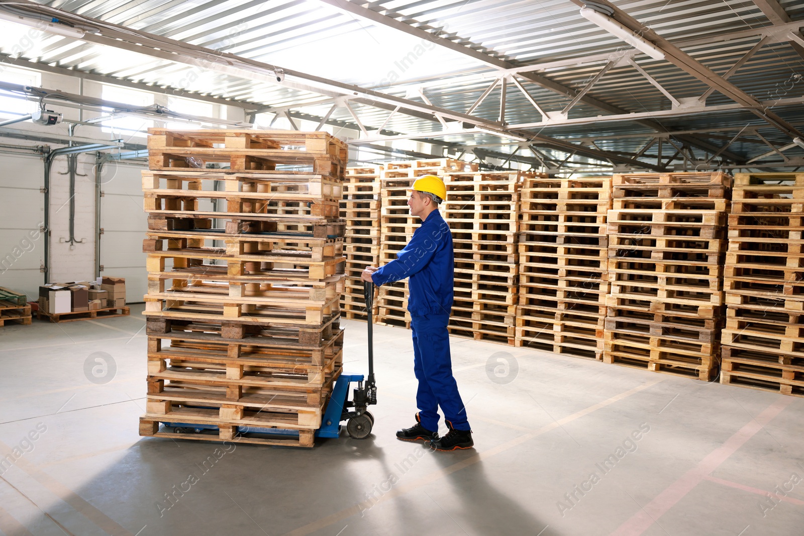 Image of Worker moving wooden pallets with manual forklift in warehouse