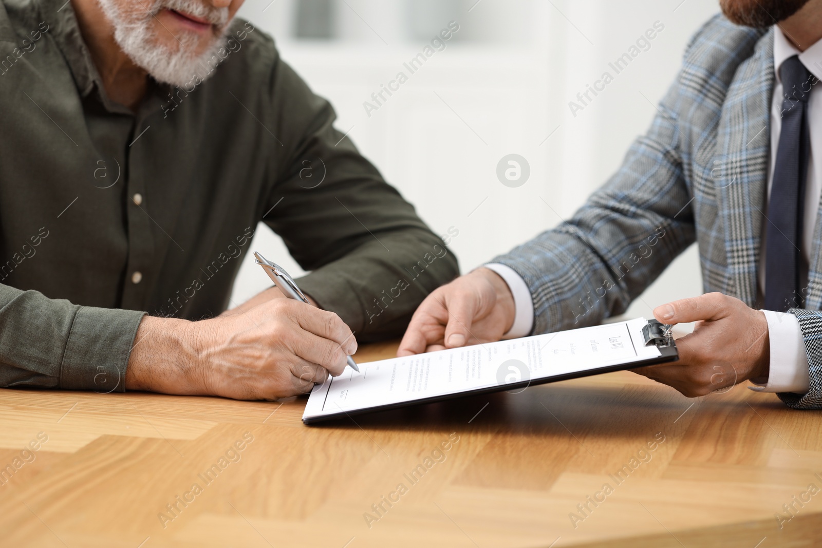 Photo of Notary showing senior man where to sign Last Will and Testament at wooden table indoors, closeup