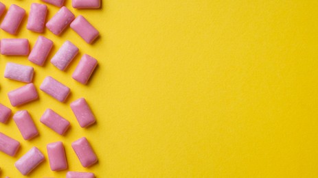 Photo of Sweet chewing gums on yellow background, flat lay. Space for text