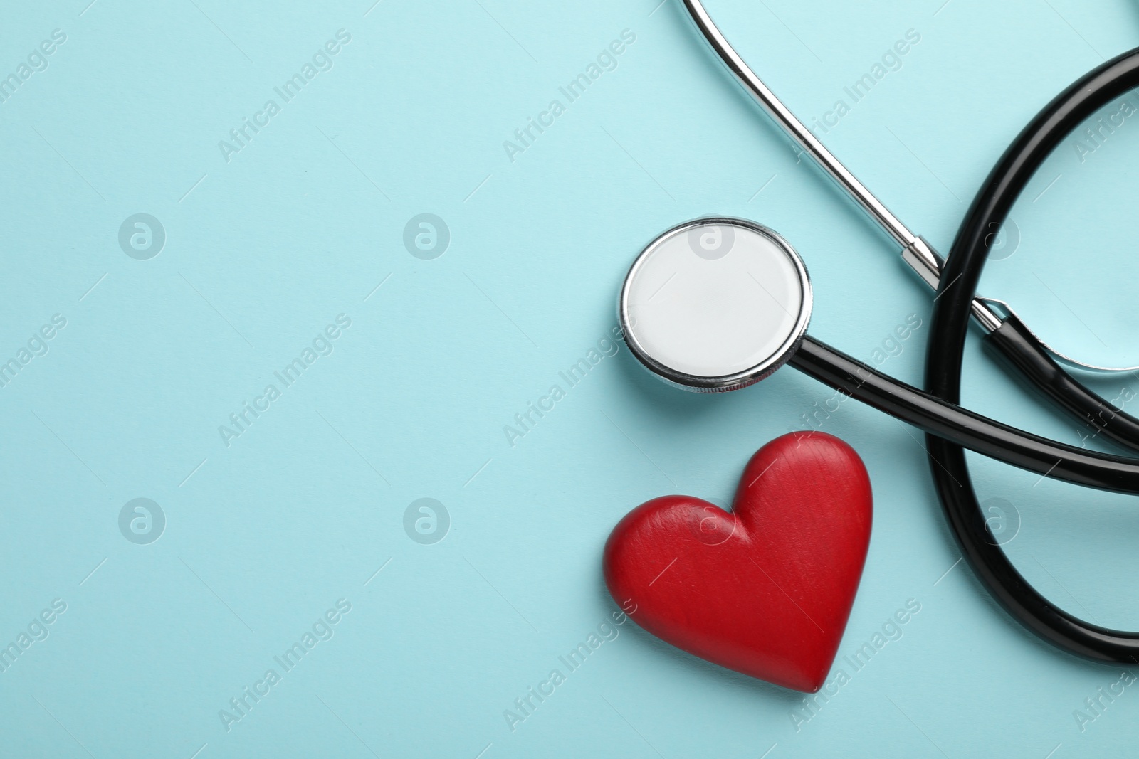 Photo of Stethoscope and red heart on light blue background, top view. Space for text