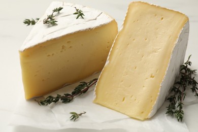 Pieces of tasty camembert cheese and thyme on white table, closeup