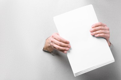 Man holding sheets of paper through holes in white paper, closeup. Mockup for design