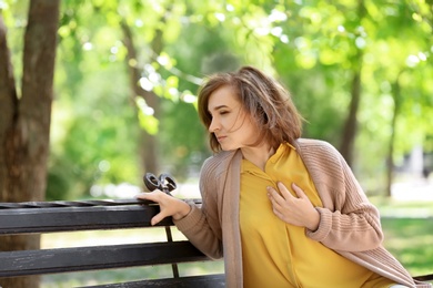 Mature woman having heart attack on bench in park