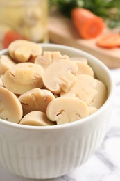 Delicious marinated mushrooms in bowl on white marble table, closeup