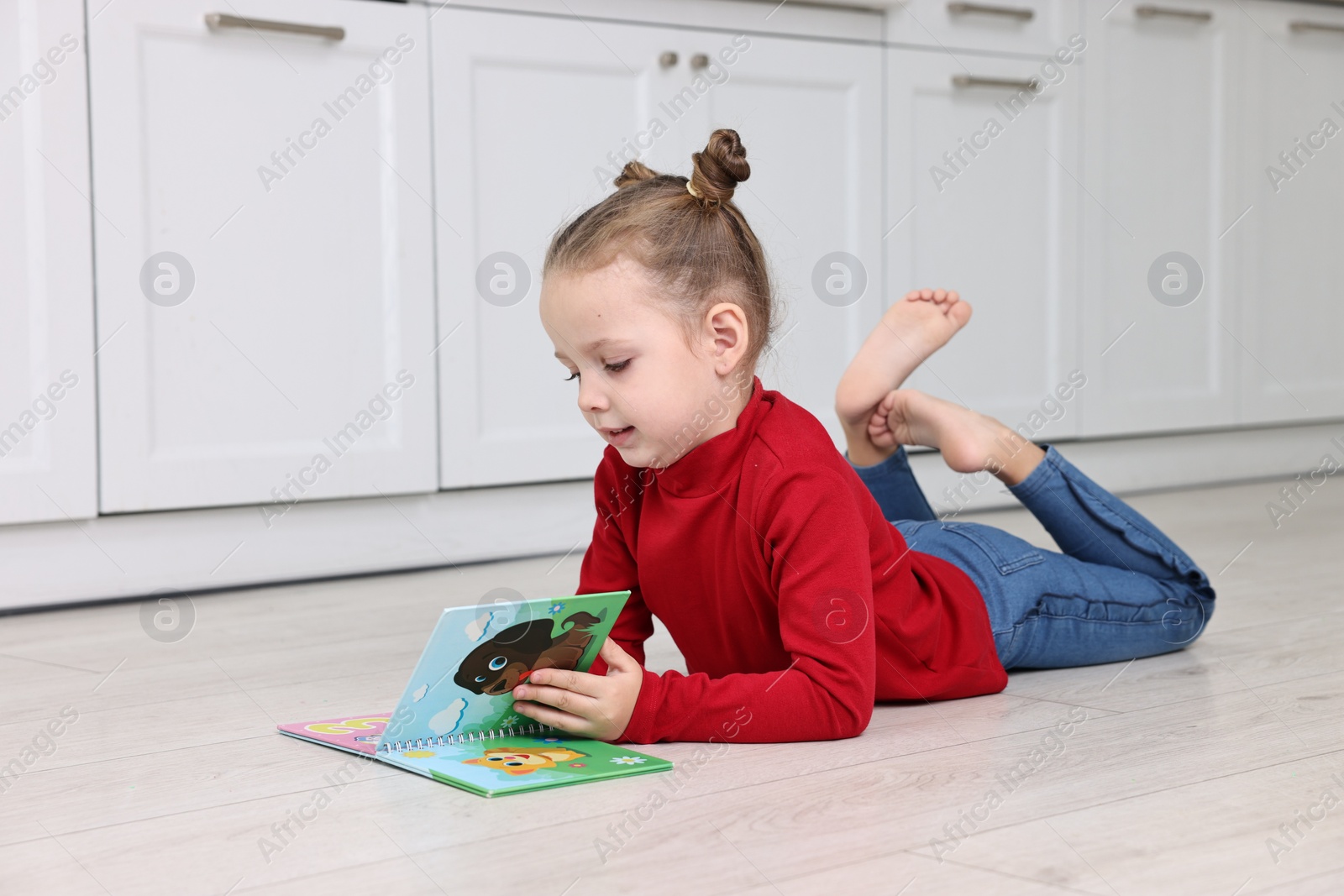 Photo of Cute little girl reading book on warm floor in kitchen, space for text. Heating system