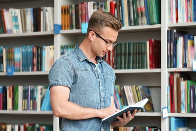 Photo of Young man with book near shelving unit in library