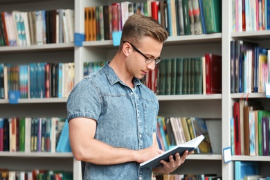 Young man with book near shelving unit in library