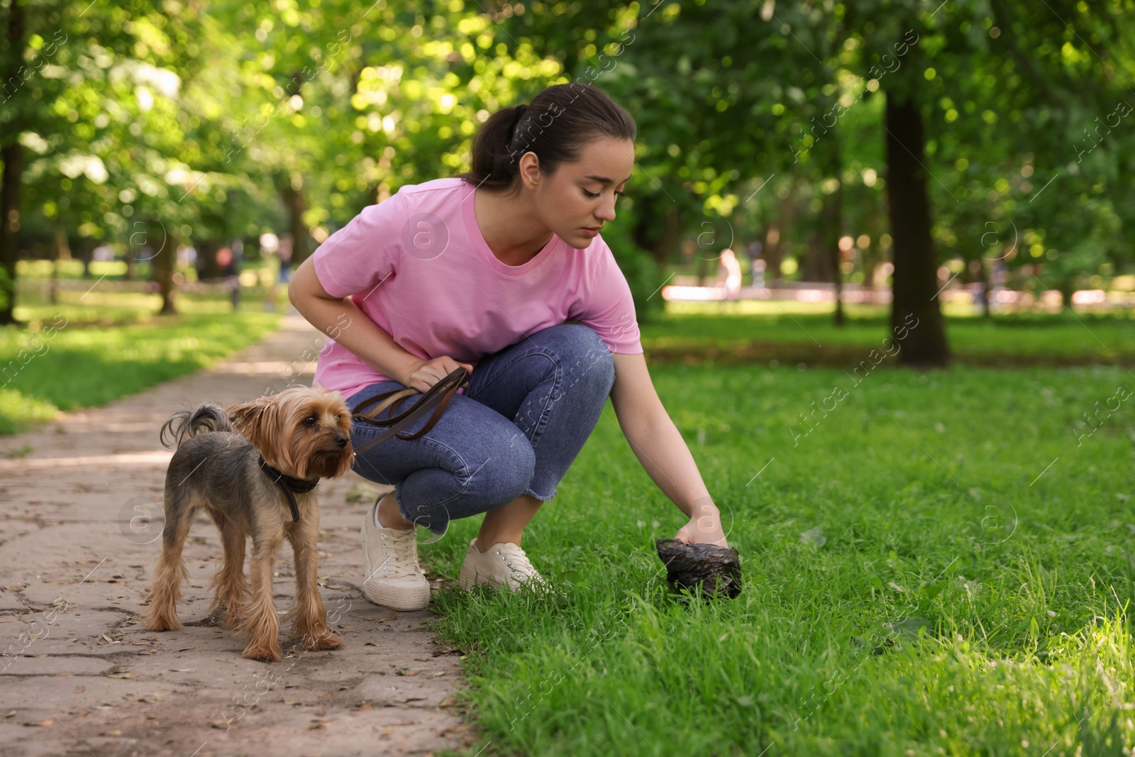 Photo of Woman picking up her dog's poop from green grass in park