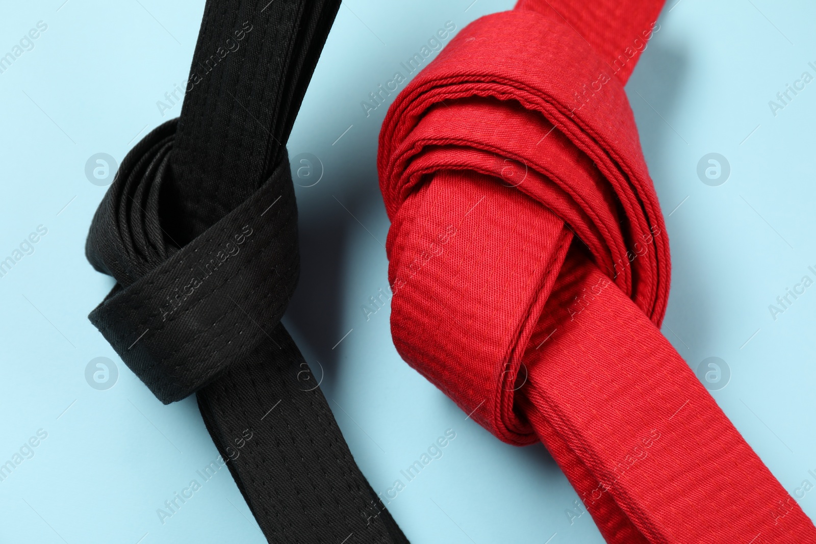 Photo of Red and black karate belts on light blue background, closeup