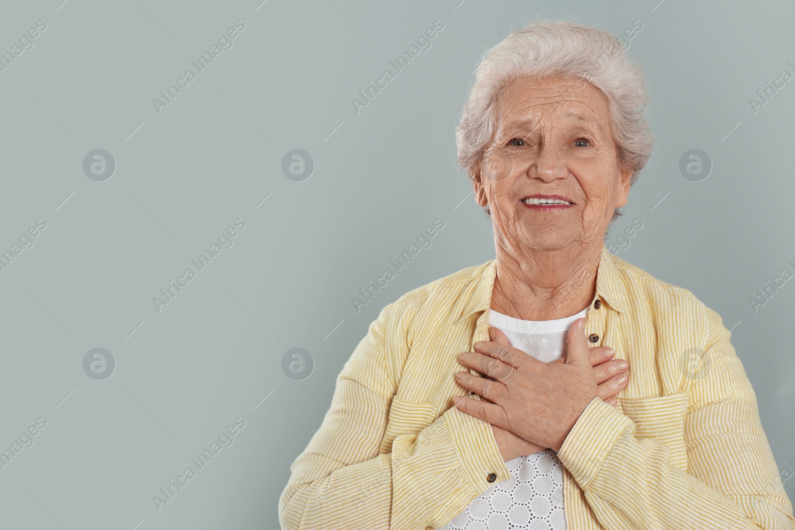 Photo of Grateful senior woman with hands on chest against grey background. Space for text