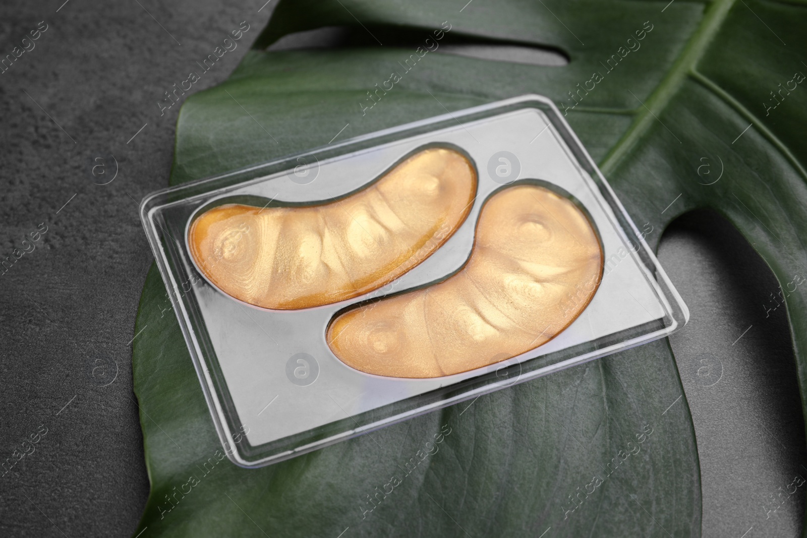 Photo of Gold under eye patches and tropical leaf on grey table. Cosmetic product