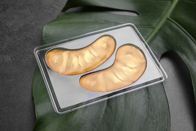 Gold under eye patches and tropical leaf on grey table. Cosmetic product