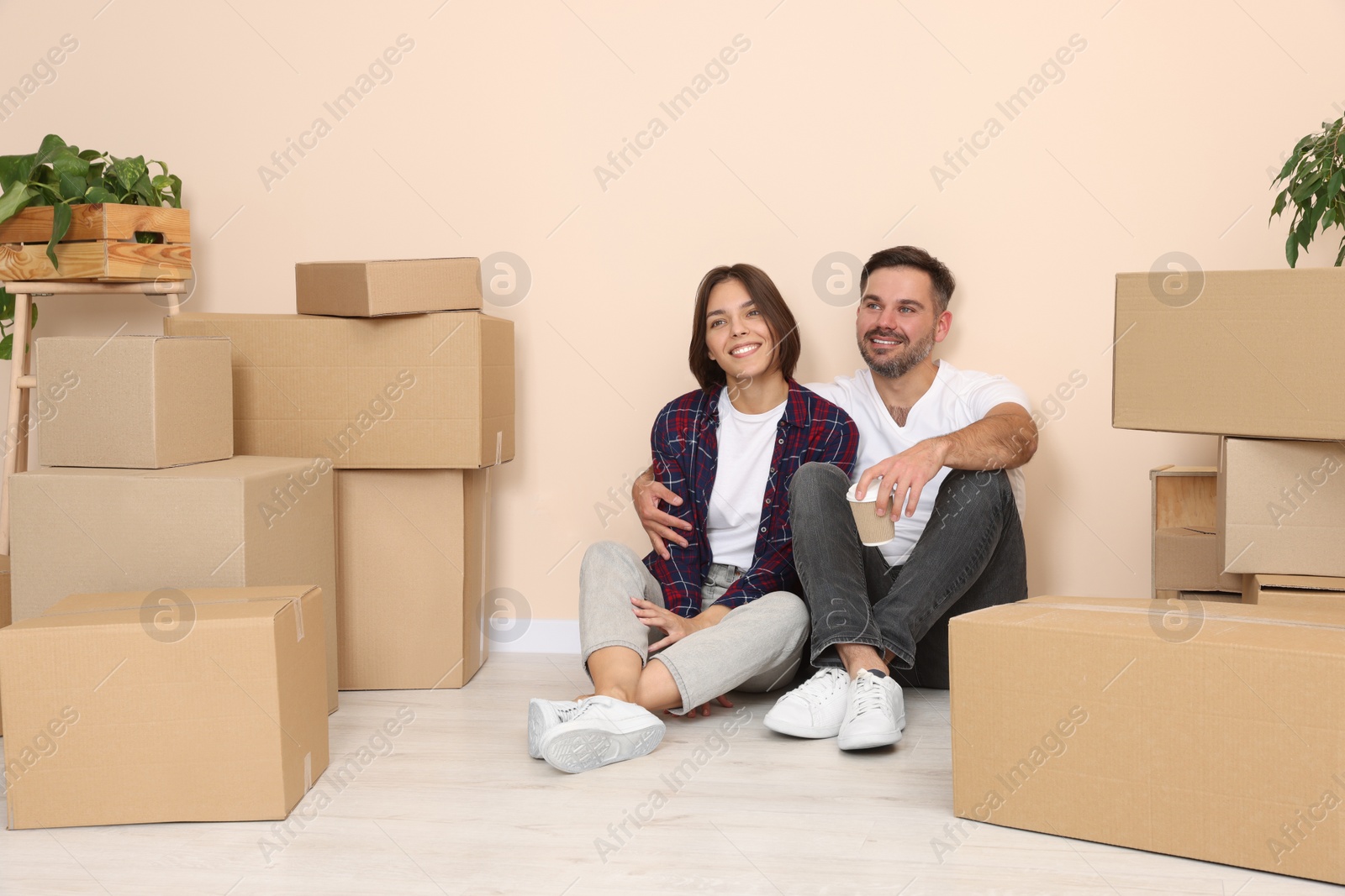 Photo of Happy couple with takeaway coffee resting on floor in new apartment. Moving day