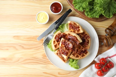 Photo of Tasty Belgian waffles served with bacon, lettuce and sauces on wooden table, flat lay. Space for text