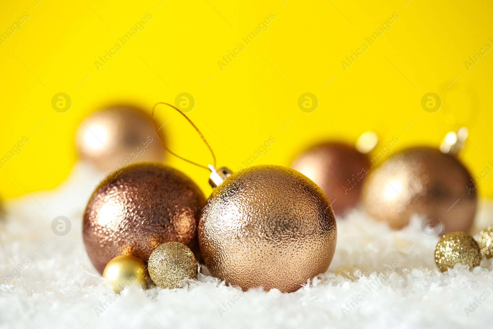 Photo of Beautiful Christmas balls on snow against yellow background. Space for text