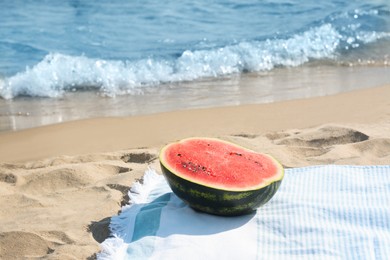 Photo of Half of fresh juicy watermelon on beach blanket near sea