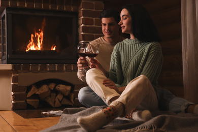 Photo of Lovely couple with glasses of wine near fireplace indoors. Winter vacation