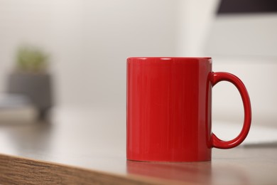 Red ceramic mug on wooden table at workplace. Space for text