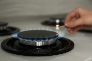 Photo of Woman lighting gas stove with match, closeup