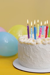 Delicious cake with burning candles and festive decor on yellow background, closeup