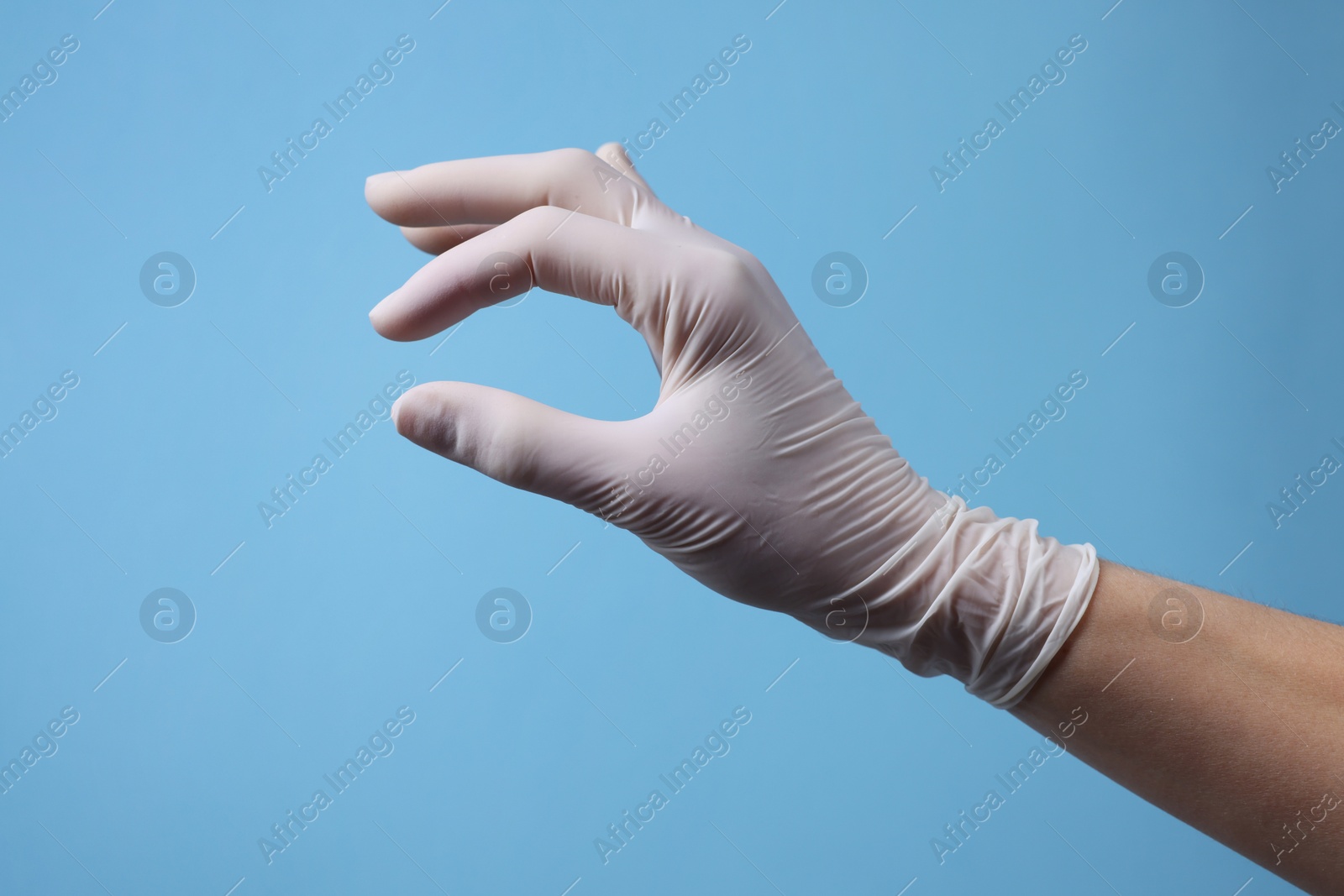 Photo of Doctor wearing white medical glove holding something on light blue background, closeup