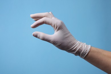 Photo of Doctor wearing white medical glove holding something on light blue background, closeup