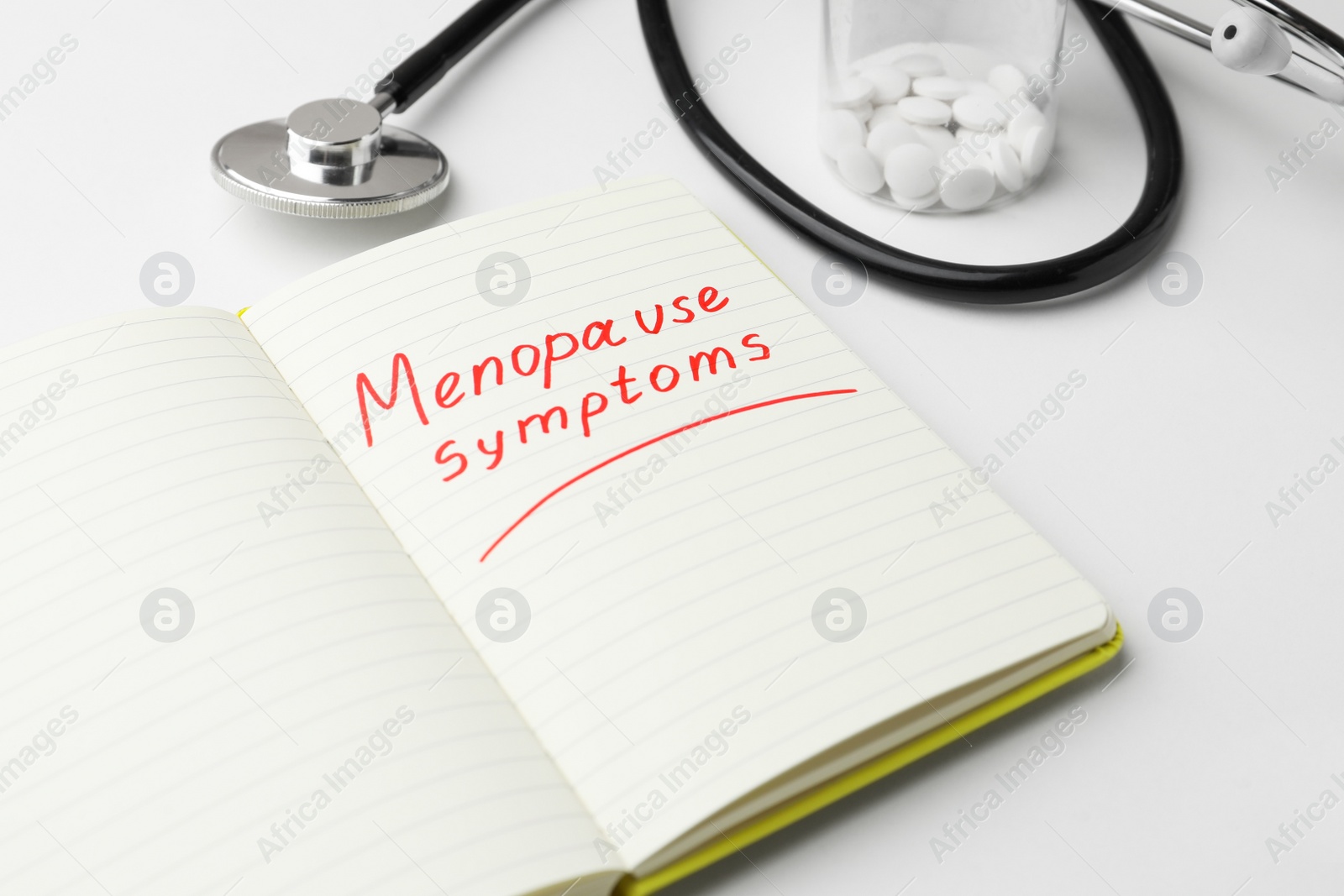 Photo of Notebook with words Menopause Symptoms, pills and stethoscope on white table