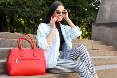 Photo of Young woman with stylish bag talking on phone outdoors