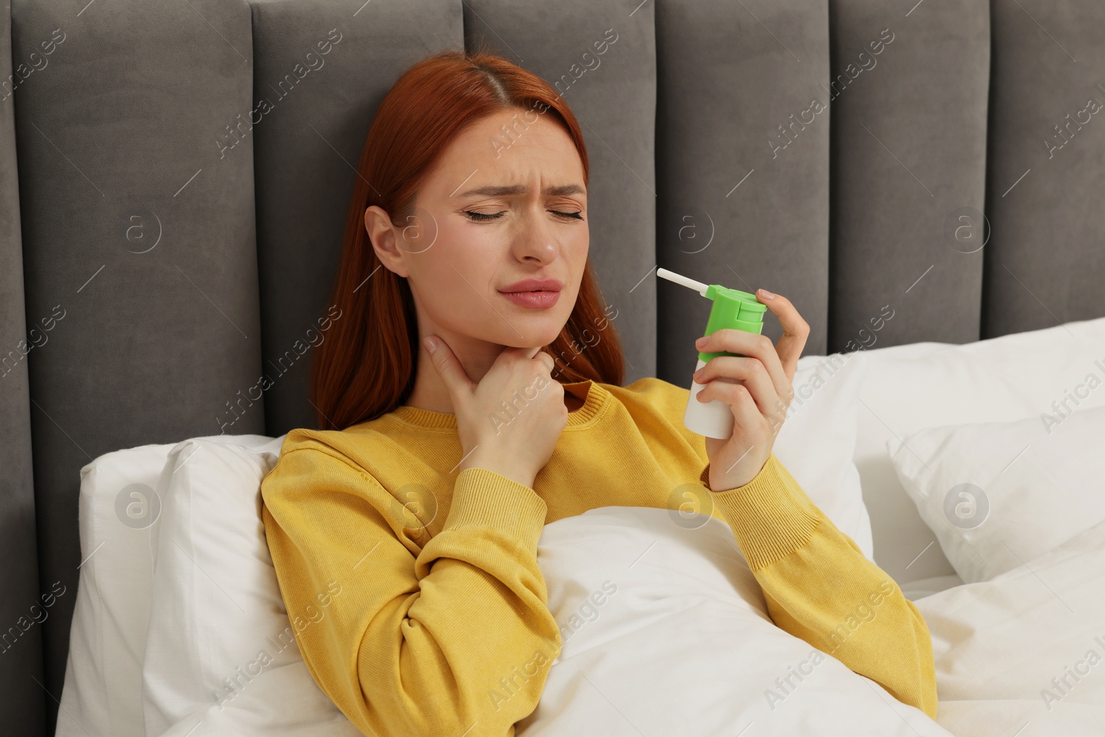 Photo of Young woman holding throat spray in bed