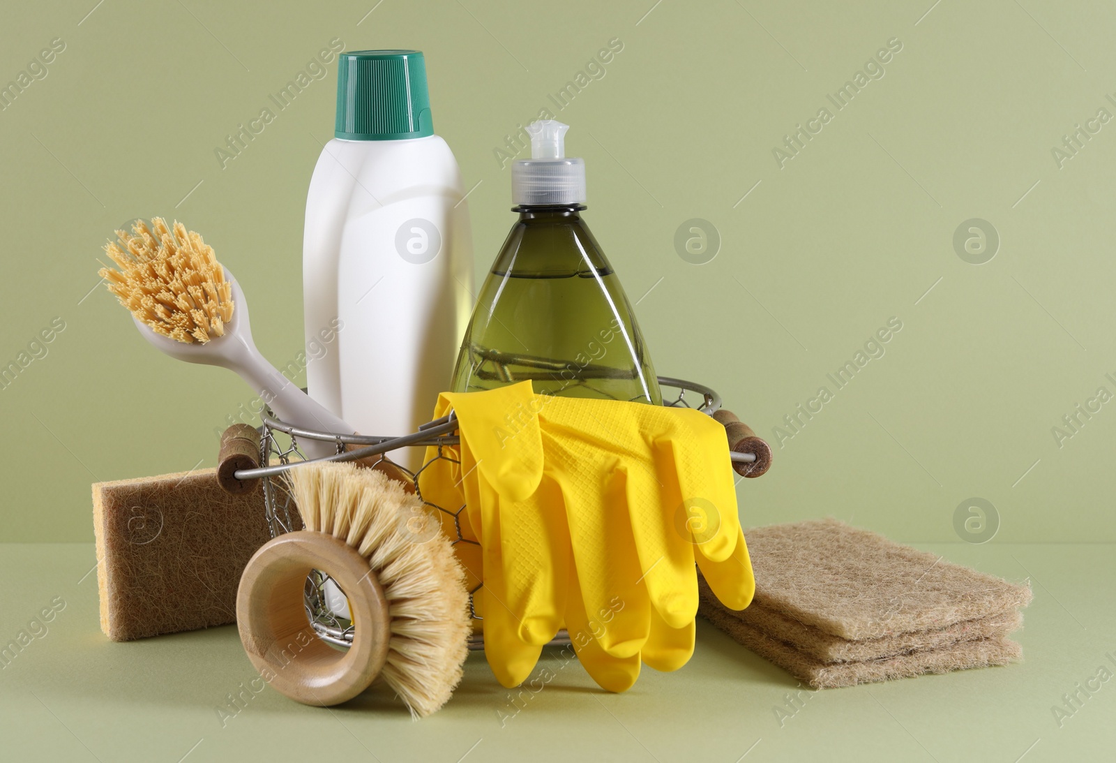 Photo of Set of different cleaning supplies in basket on light green background