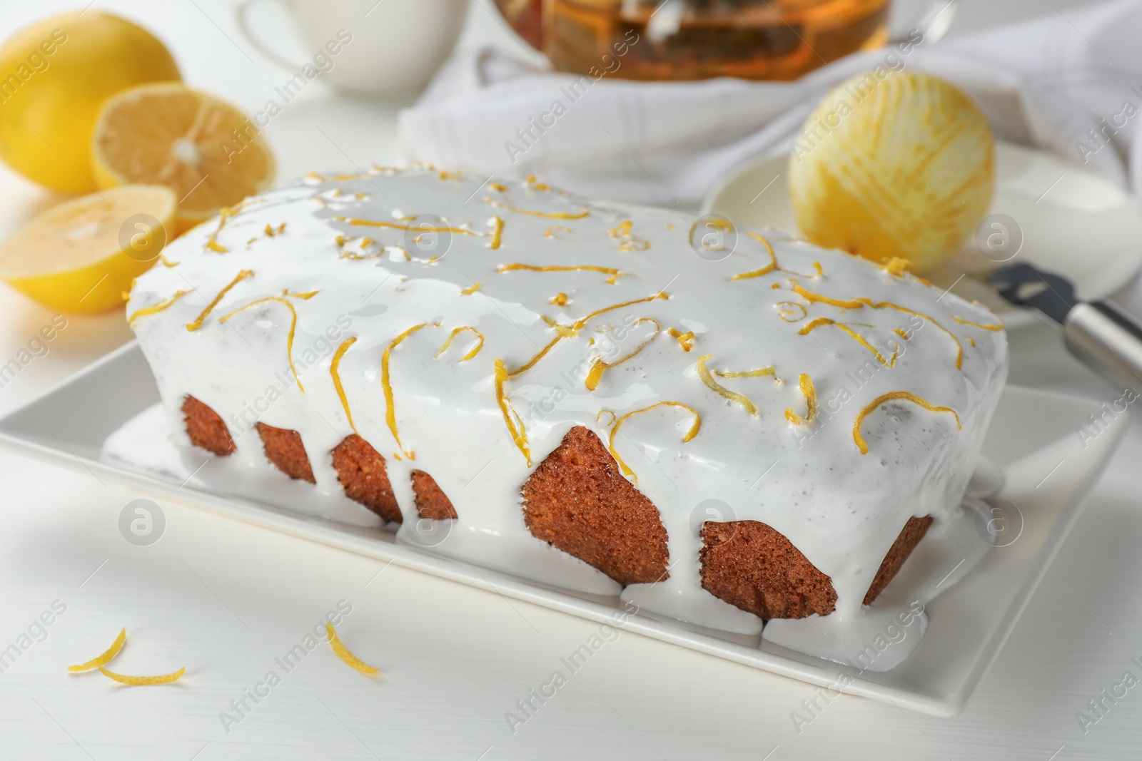 Photo of Tasty lemon cake with glaze and citrus fruits on white table