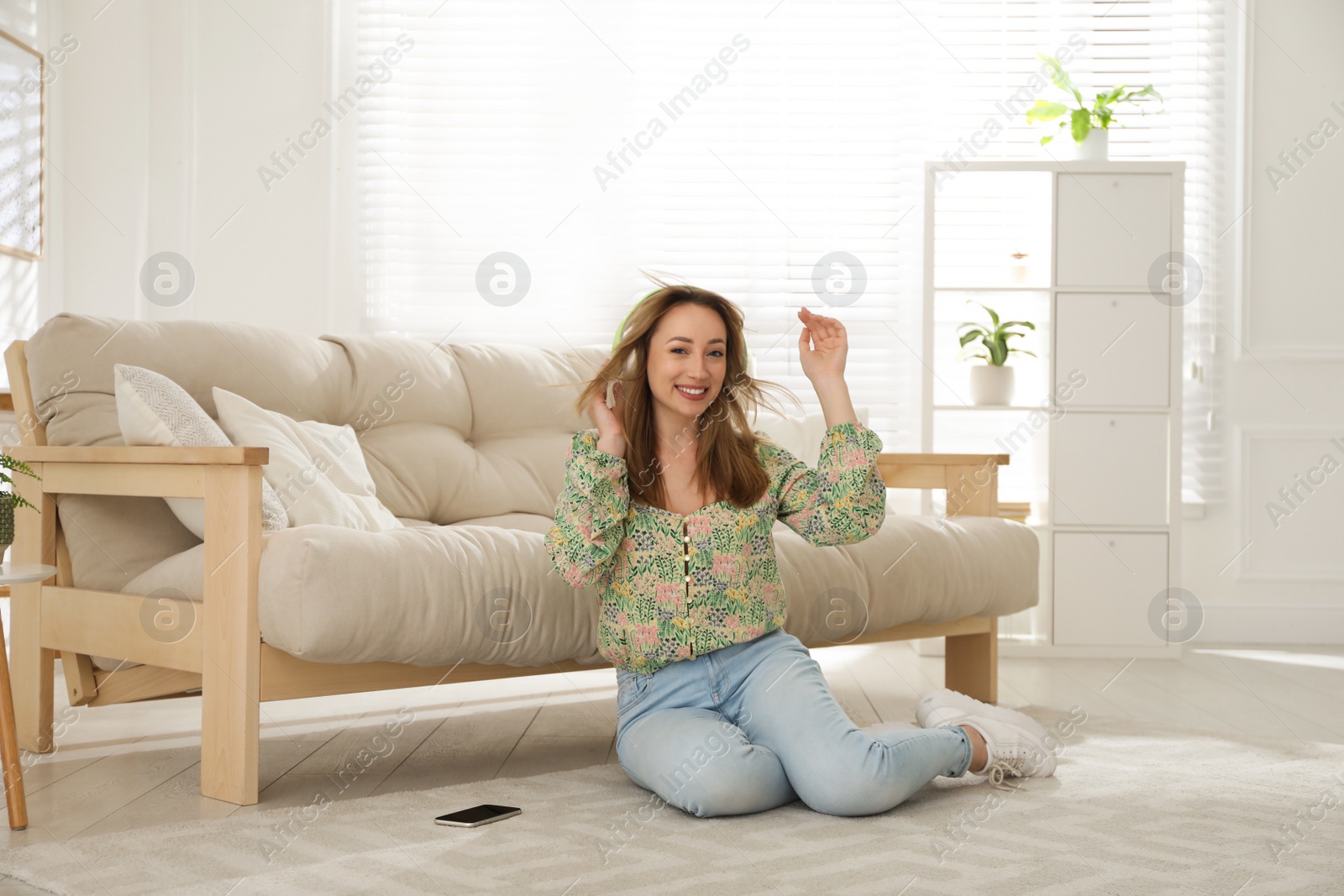 Photo of Young woman with headphones listening to music while sitting on floor in living room