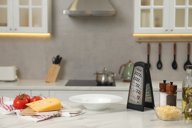 Photo of Grater, delicious cheese and other products on white marble table in kitchen