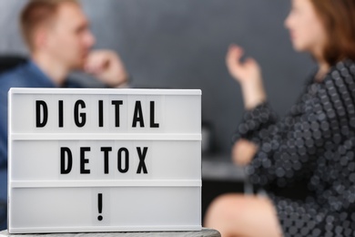 Colleagues chatting in office, focus on lightbox with phrase DIGITAL DETOX