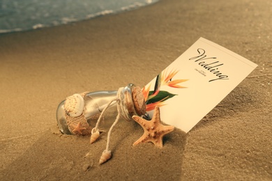 Photo of Wedding invitation and glass bottle on sandy beach at sunset