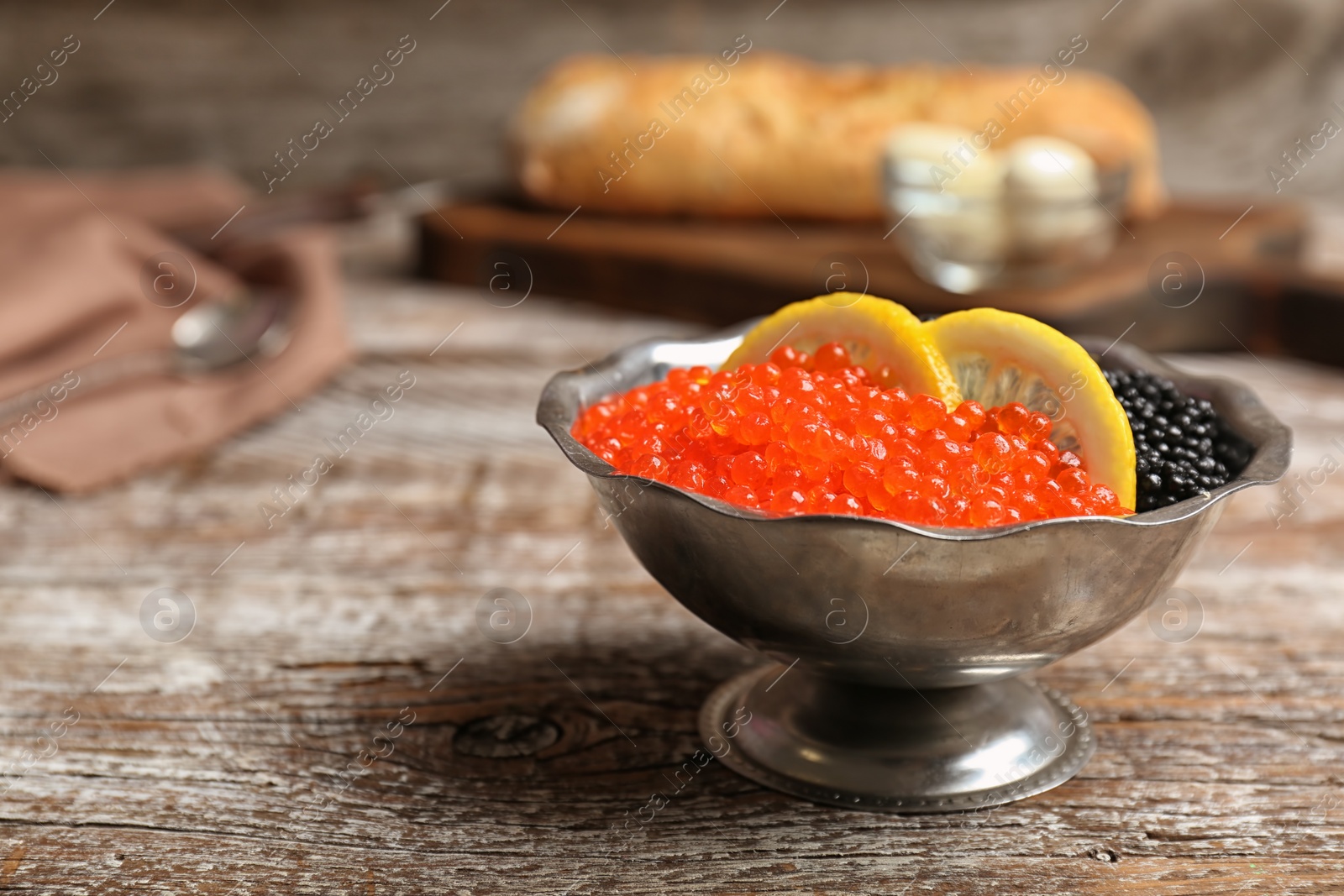 Photo of Metal bowl with black and red caviar on wooden table